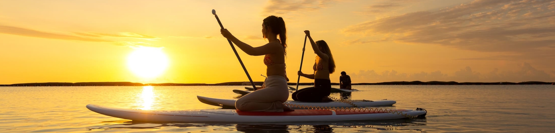 Two women paddleboarding at sunset