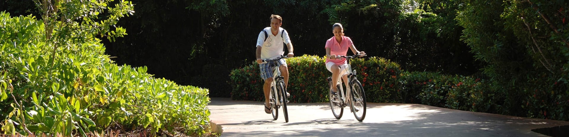 A couple rising bikes along a road surrounded by greenery.