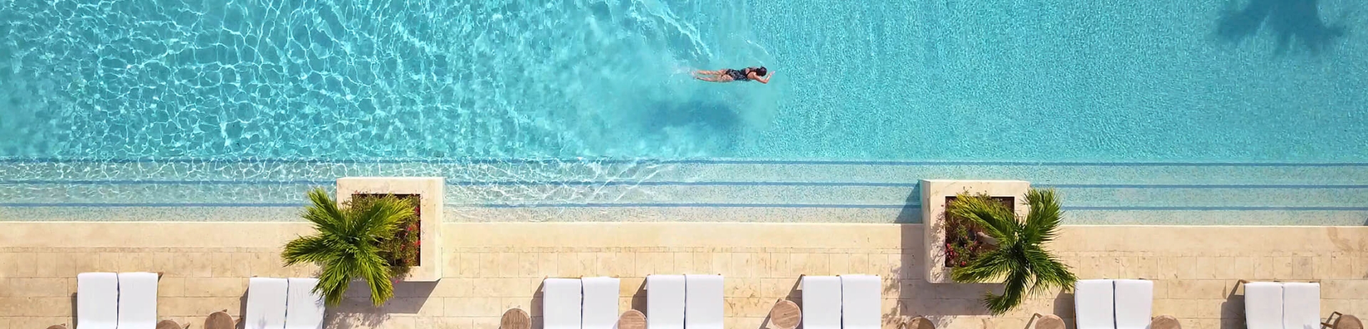 An aerial view of a woman swimming the length of a large outdoor swimming pool.