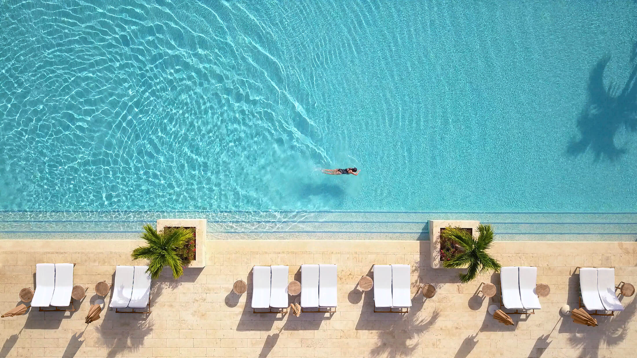 An aerial view of a woman swimming the length of a large outdoor swimming pool.