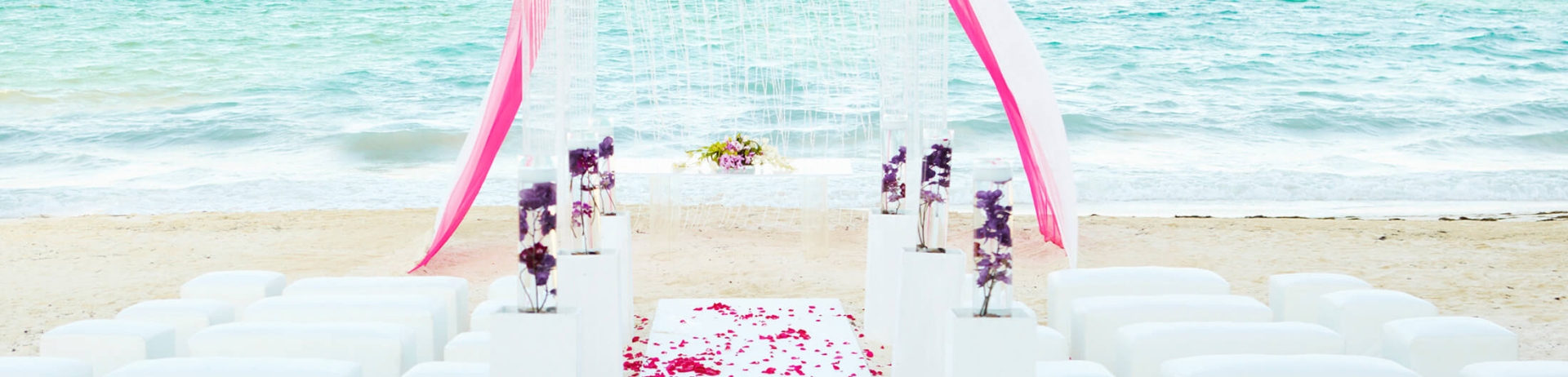 A an oceanfront beach wedding aisle and archway decorated in white and pink