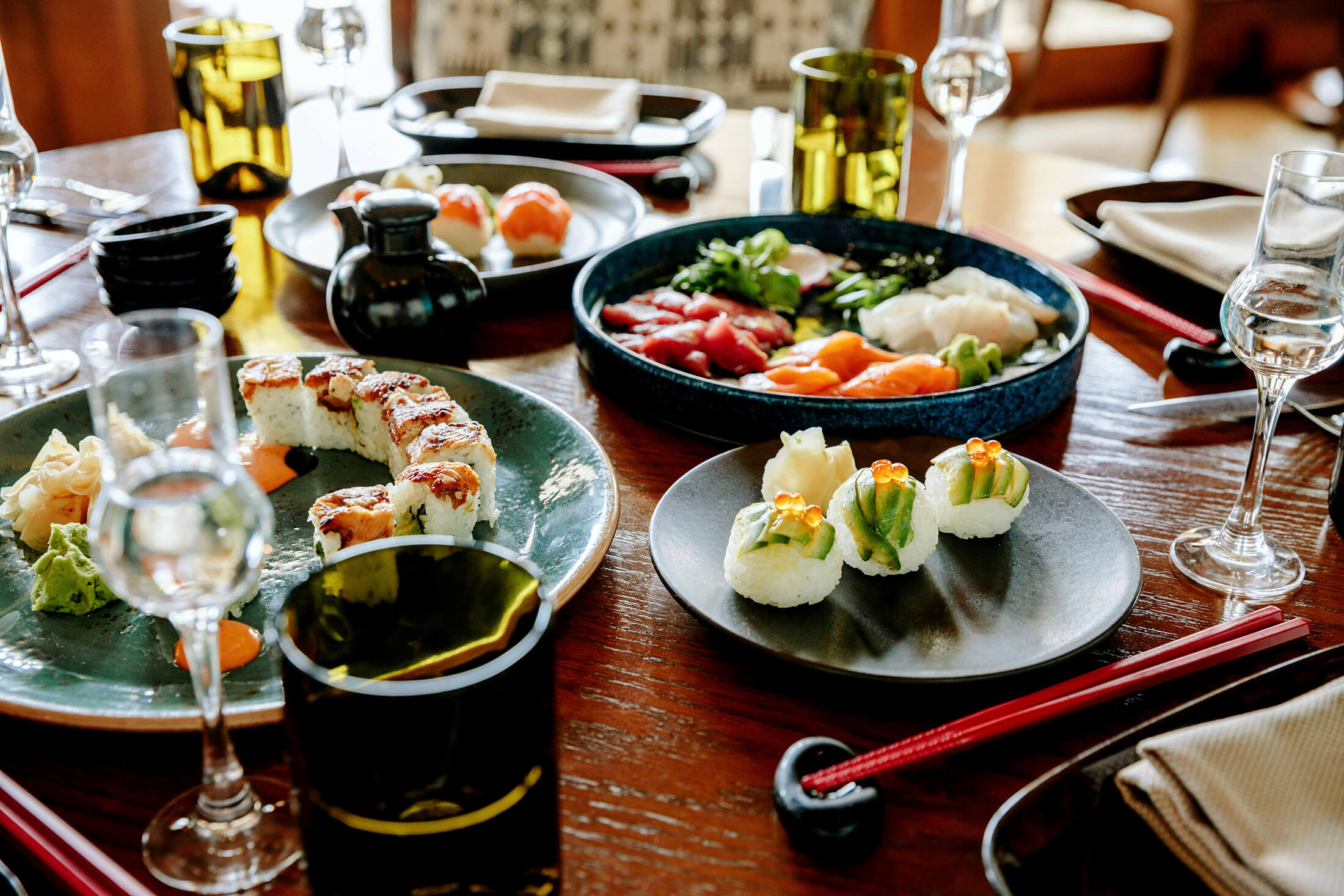 A dinner table loaded with plates of sushi, sashimi, and beverages.