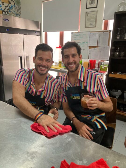 Two men in striped shirts and aprons sitting at a metal table.