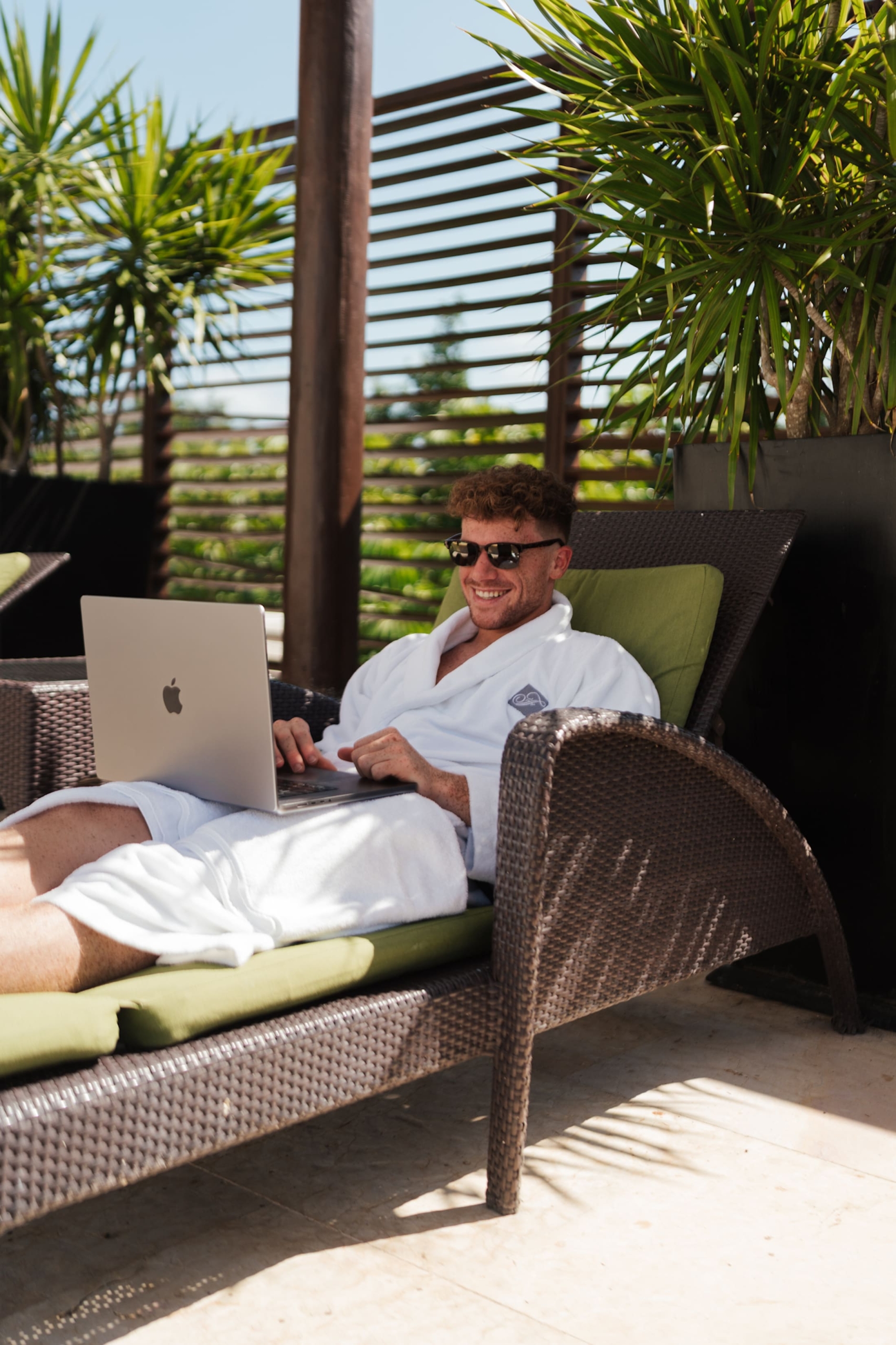 A man in a white robe on a pool lounger with a laptop in his lap.