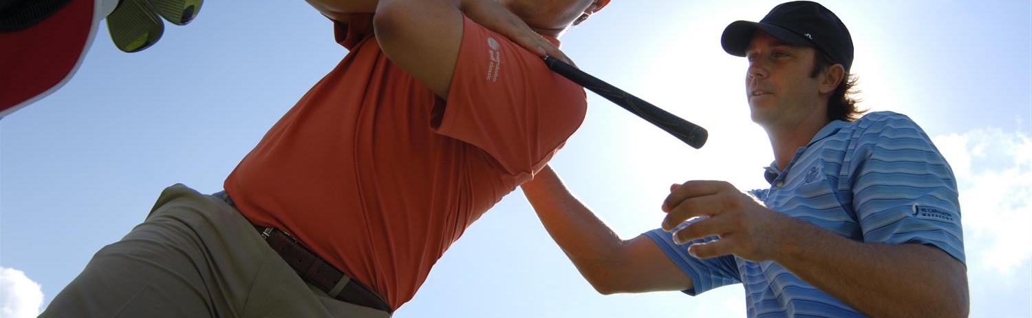 A golf pro coaching a man on a golf course.
