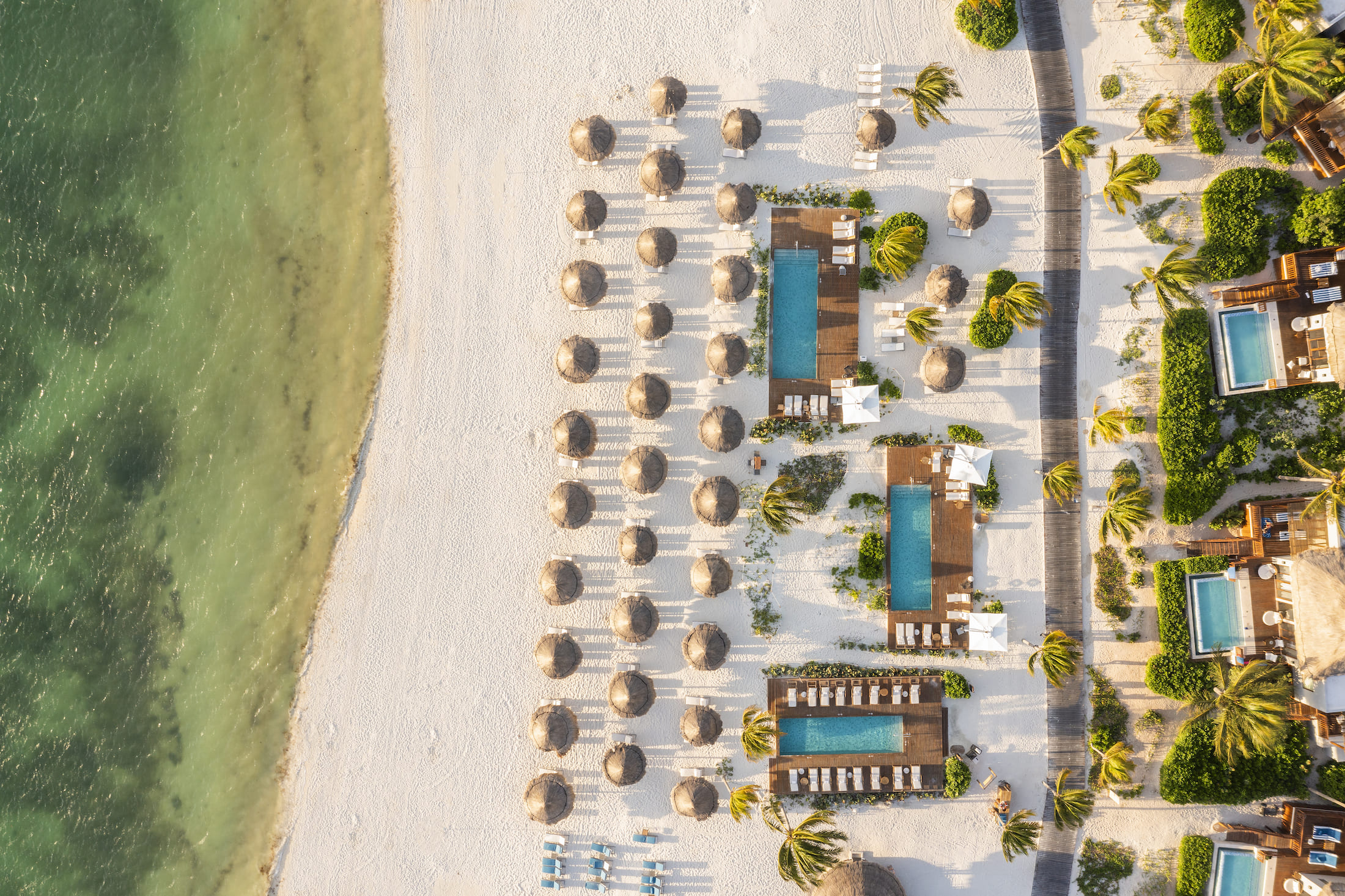 Aerial view of Fairmont Mayakoba's beach line with huts and infinity pools.